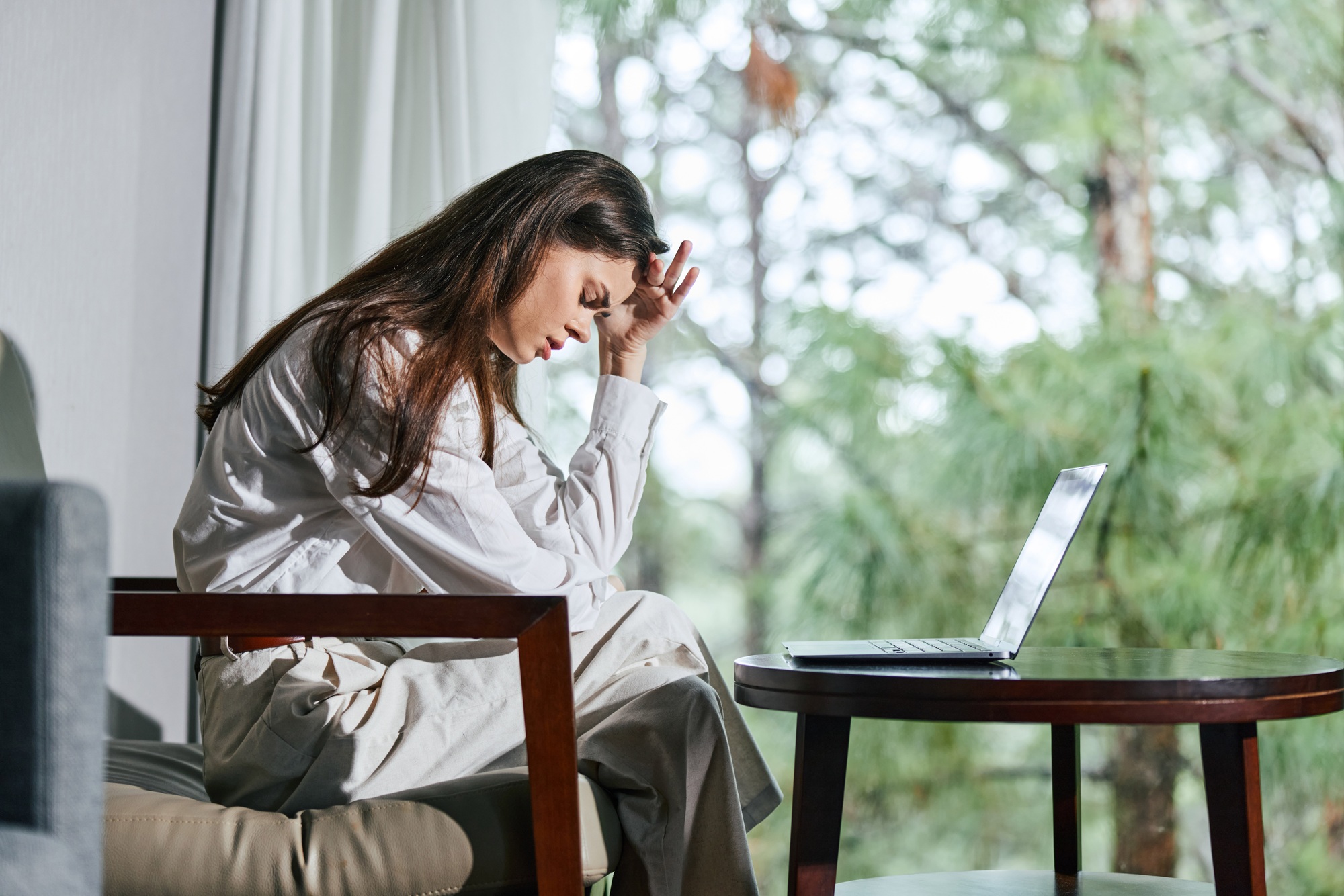 Eine gestresste Frau sitzt an ihrem Laptop und fühlt sich von ihrer Arbeit überwältigt, umgeben von einer ruhigen Natur